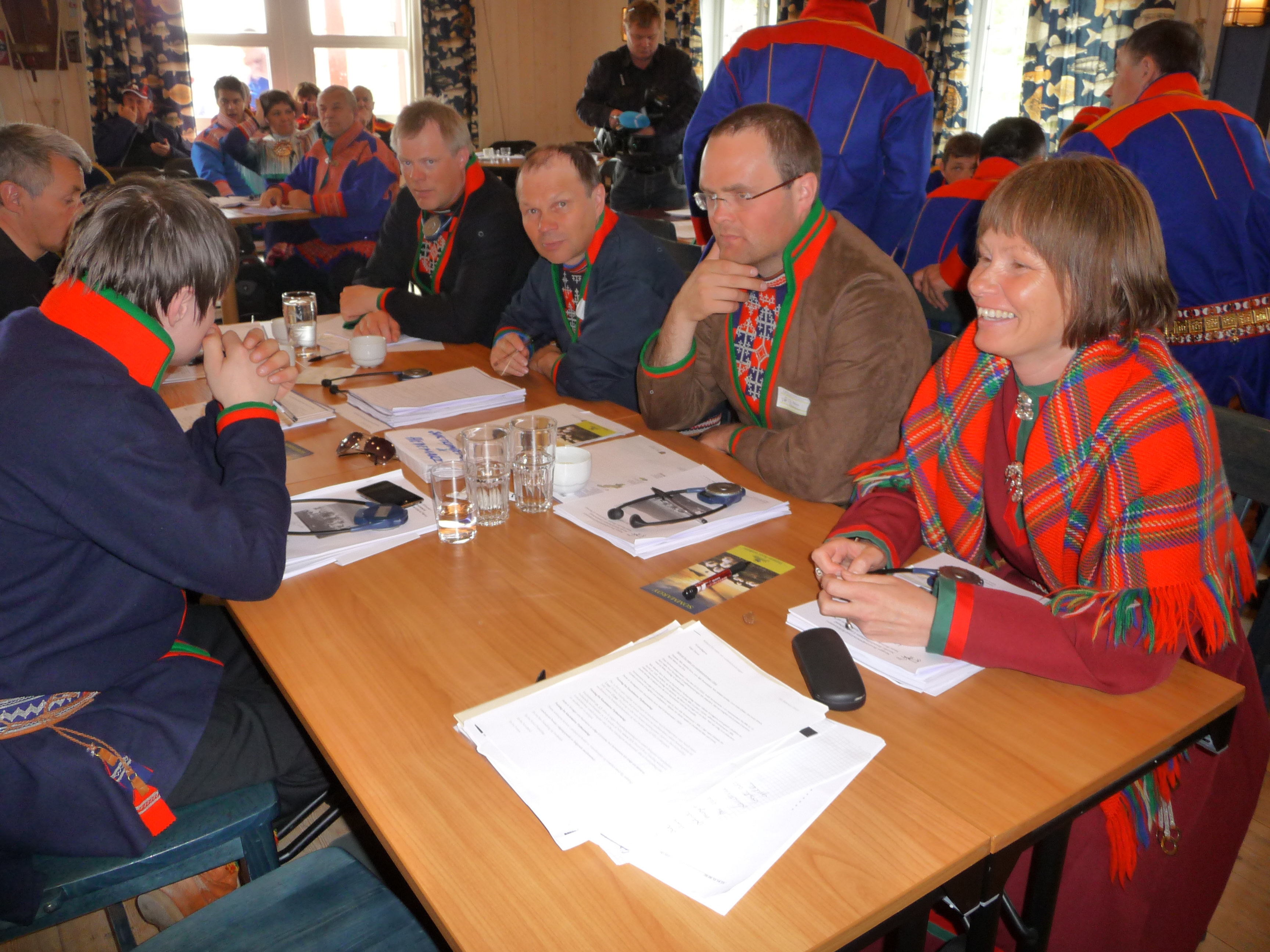 Personer kledd i samisk drakter rundt et bord. Foto.