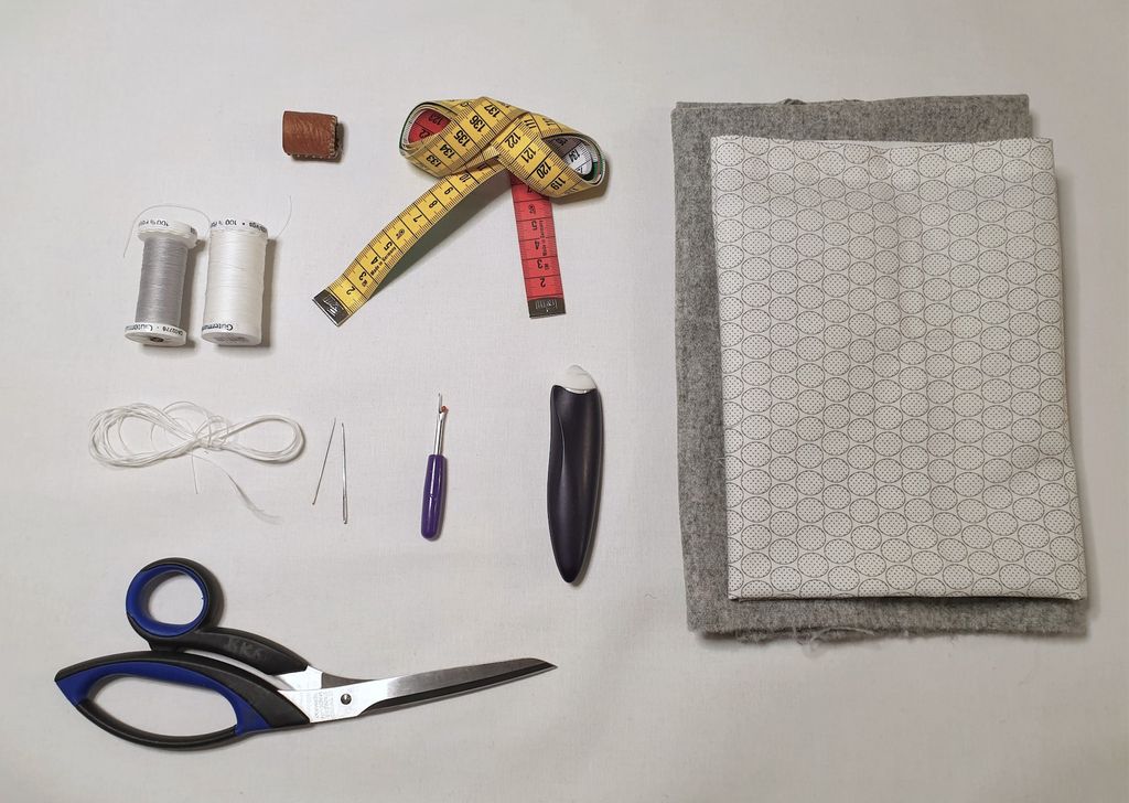 Fotografi av fingerbøl, målebånd, stoff, trådsneller, nåler, sprettekniv, skredderkritt og saks.