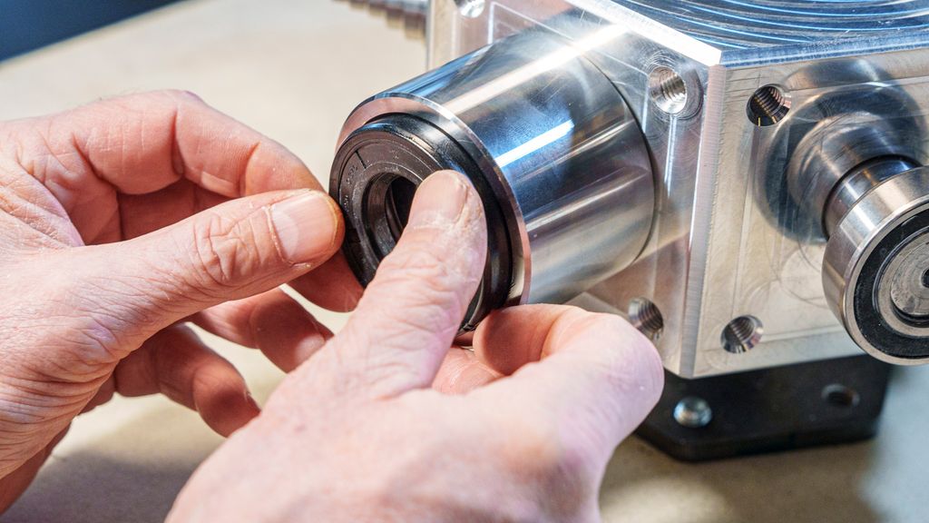 To hender som presser en sort ring mot en åpning. Foto.