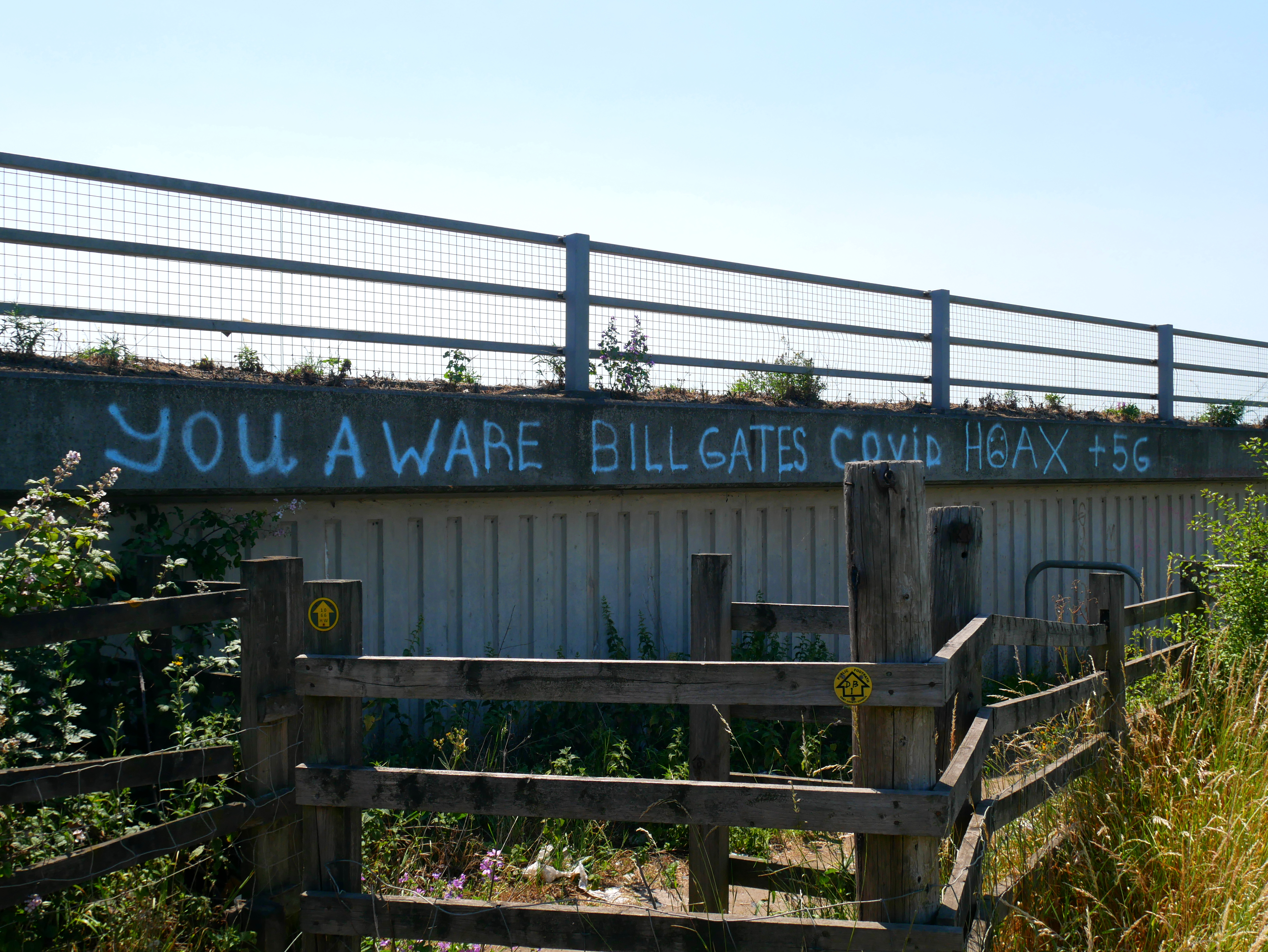 Conspiracy theory graffiti tagged on a building, stating the following: "you aware Bill Gates Covid hoax +5G". Photo.