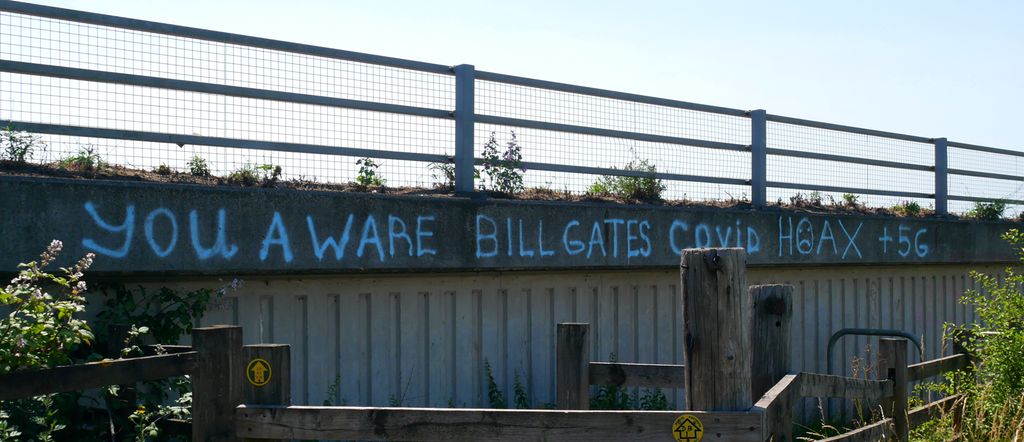 Conspiracy theory graffiti tagged on a building, stating the following: "you aware Bill Gates Covid hoax +5G". Photo.
