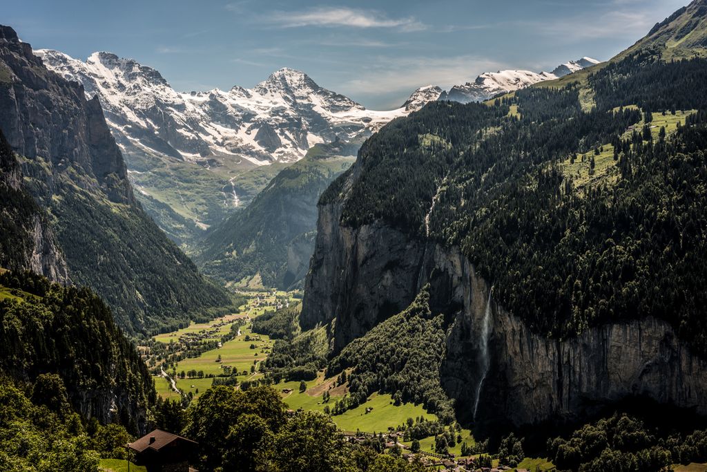 Grønt landskap i Berner Oberland, Sveist, med snødekte fjell i bakgrunnen. Spredt bebyggelse. Foto.