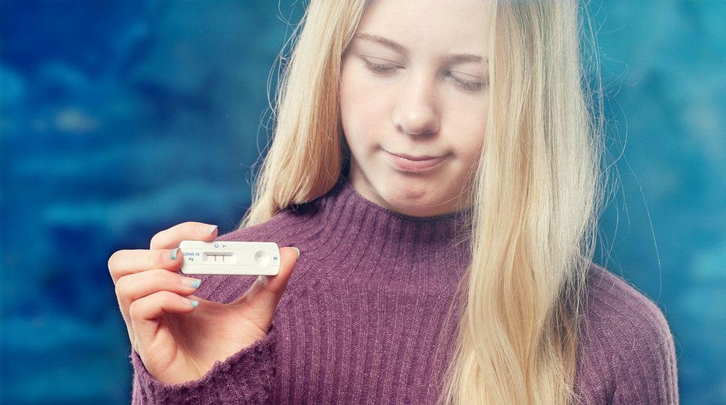 Blond jente holder opp en positiv covid-19-selvtest. Foto.