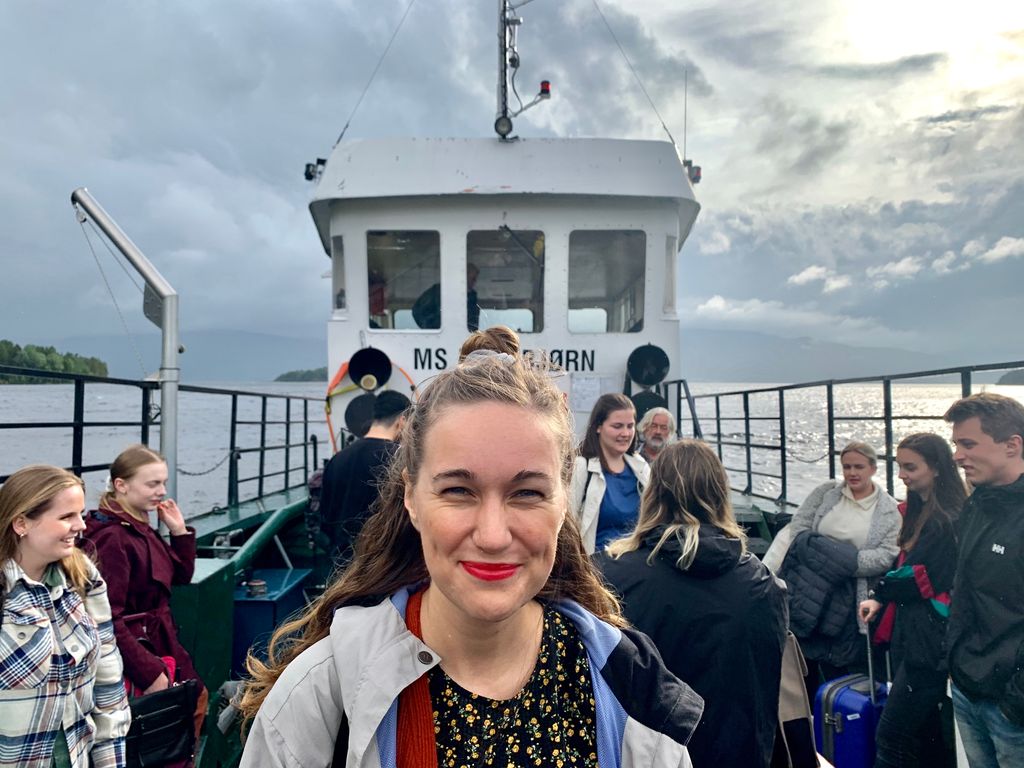 Foto av ei blid ung kvinne på ei passasjerferge. I bakgrunnen er det flere andre personer.