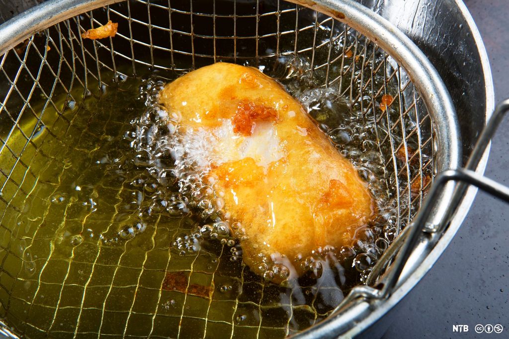 Et stykke med fisk dyppet i frityrrøre stekes i en frityr. Foto.