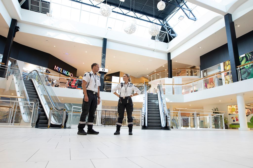 To vektere står foran rulletrapper i et kjøpesenter. Foto. 