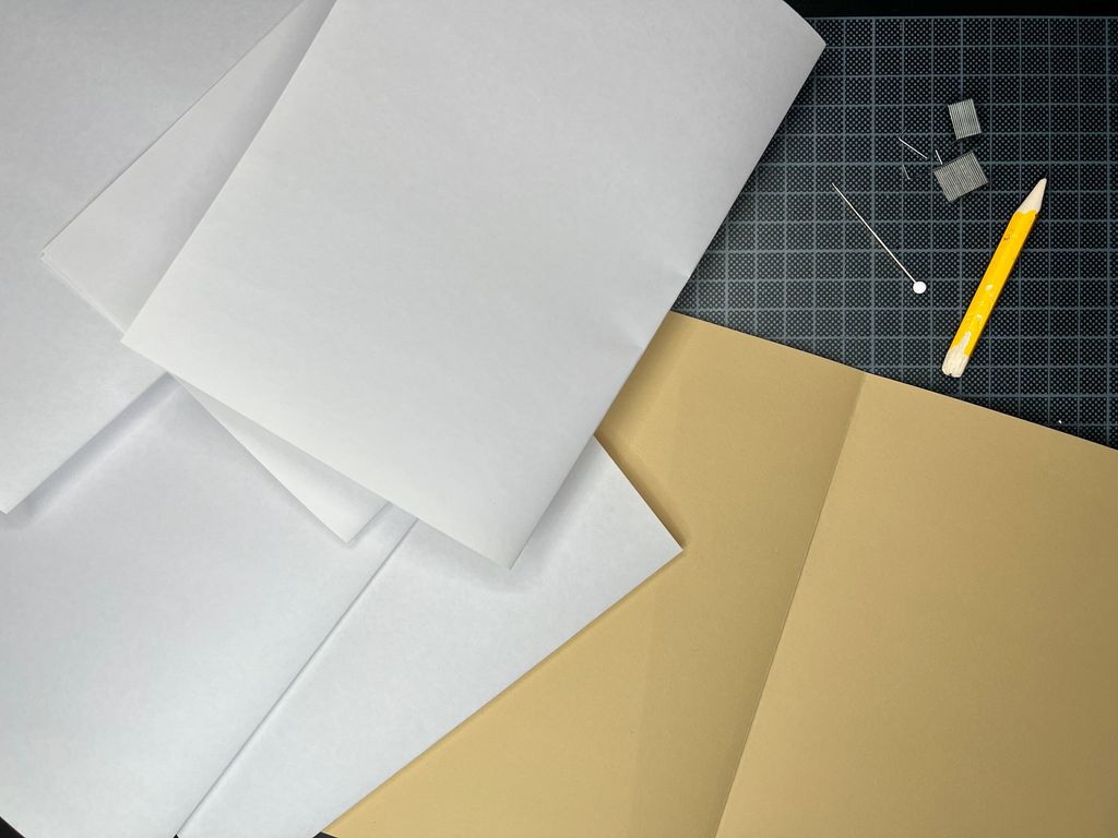 Blyant, nål og stifter ligger ved noen brettede ark. Foto.