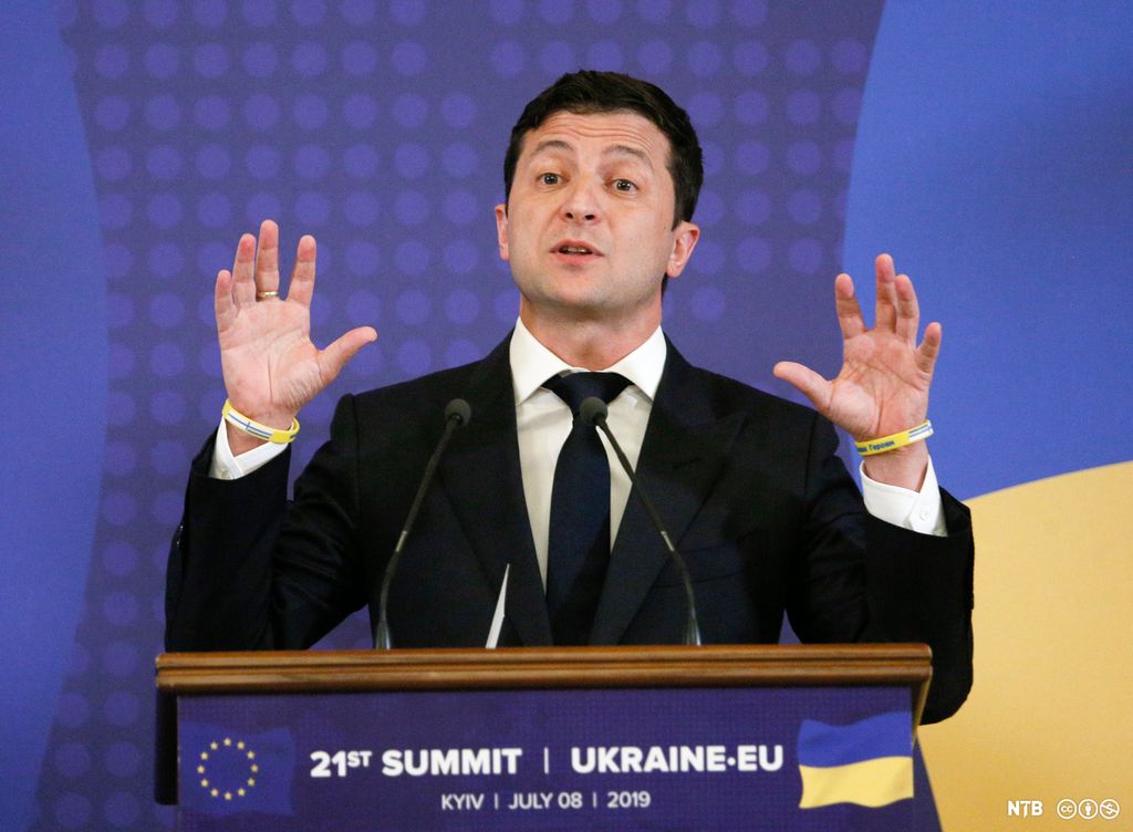 Ukrainas president Volodymyr Zelenskyj står på en talerstol i et møte mellom EU og Ukraina i 2019. Han har kort, mørkt hår og brune øyne og har på seg en mørk dress, mørkeblått slips og hvit skjorte. Foto.
