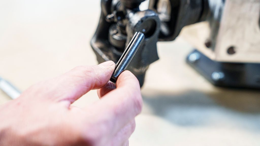 Hånd som holder en sylindrisk aksling. Foto.