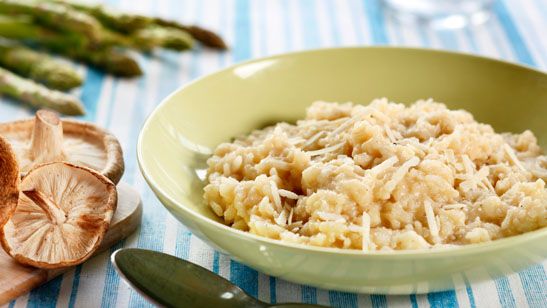 Risotto i lysegrønn skål. Sopp og grønn asparges ligger ved siden av på bordet. Foto.
