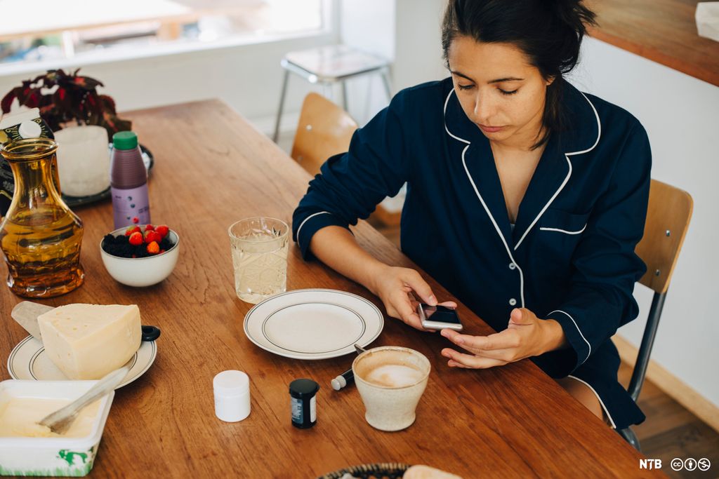 Kvinne sjekker blodsukker ved frokostbordet. Foto.