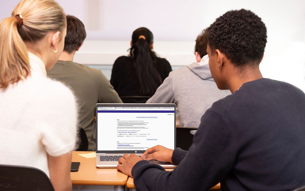 Ei jente og en gutt i et klasserom samarbeider foran en datamaskin. De sitter med ryggen til kameraet. Foto.