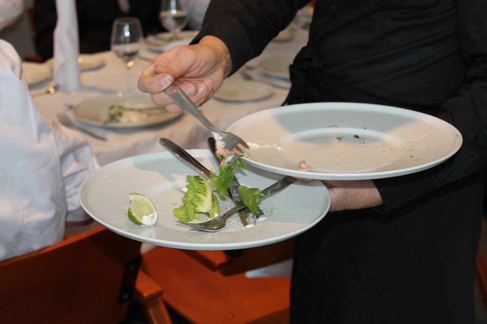 Servitør ryddar tallerkenar i ein restaurant. Foto.