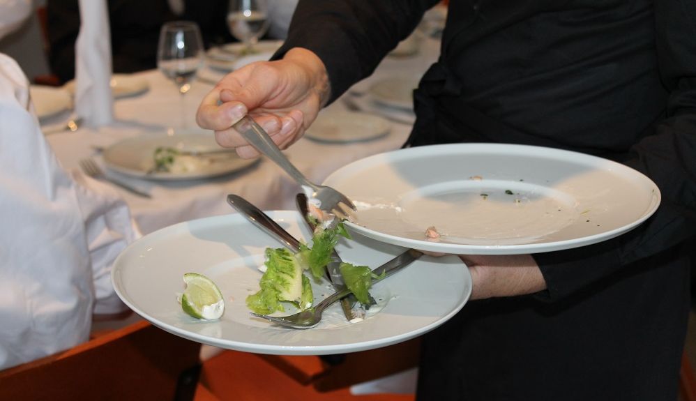 Servitør ryddar tallerkenar i ein restaurant. Foto.