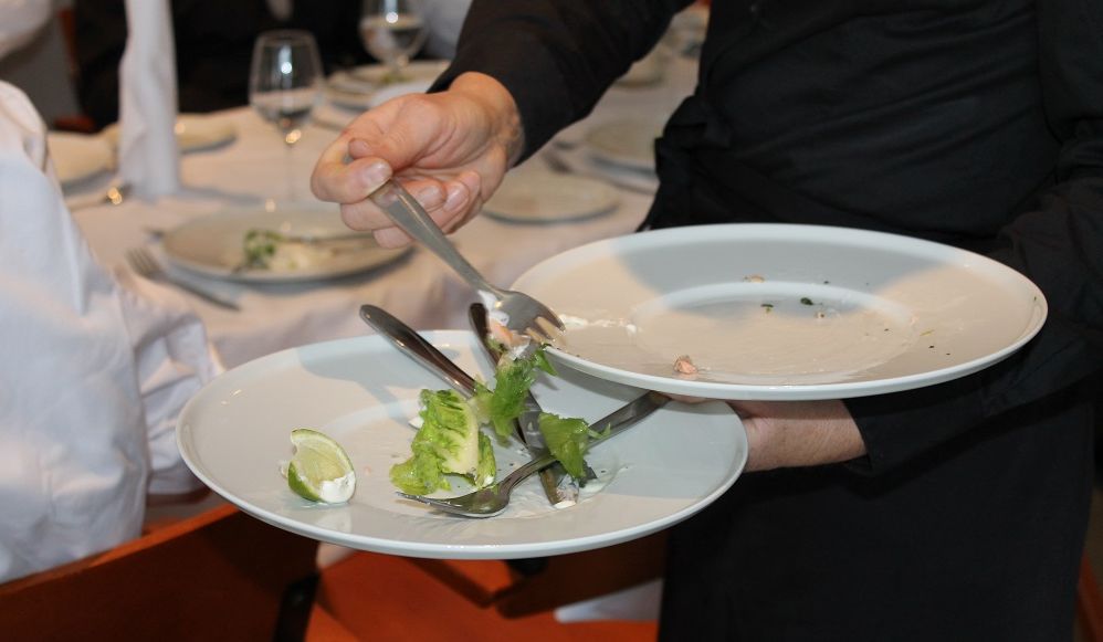 Servitør rydder tallerkener i en restaurant. Foto.