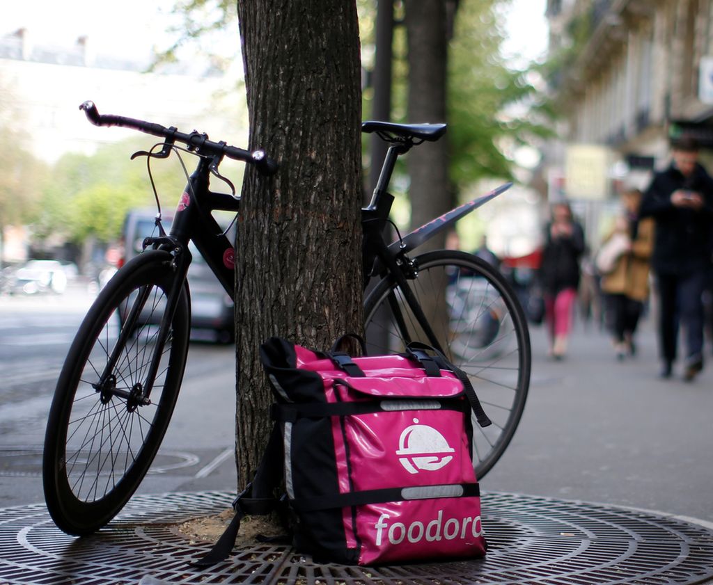 En sykkel og ei rosa veske med Foodora-logo er lent inntil et tre. Foto.