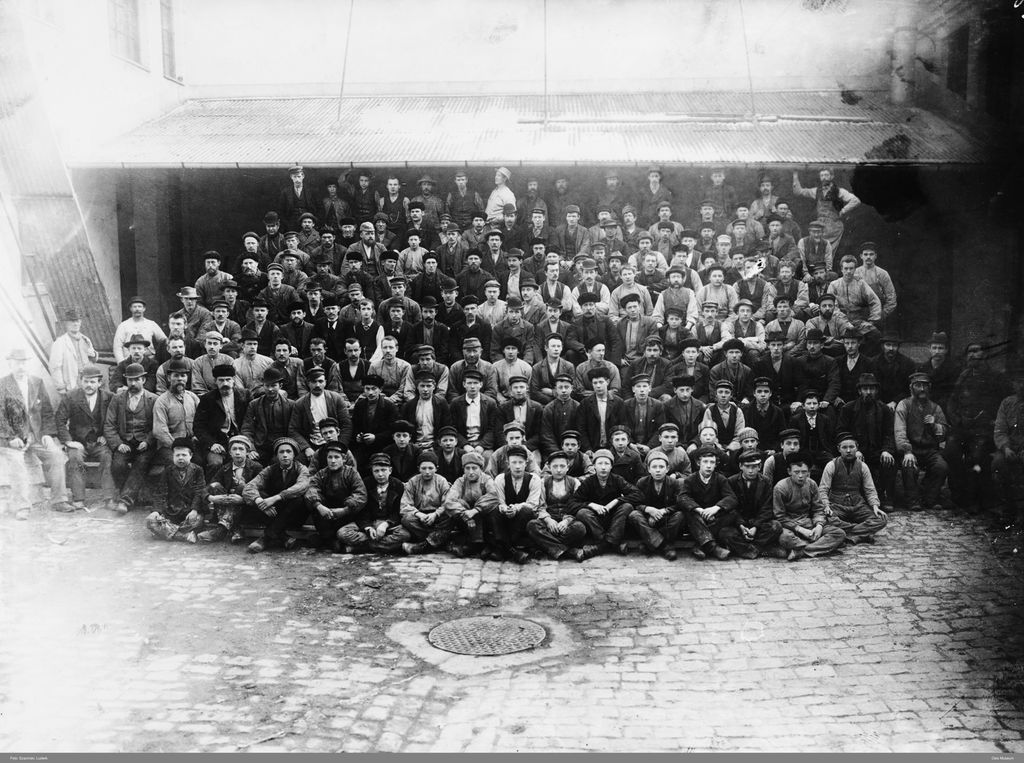 Fabrikkarbeidere ved Christiania Guldlistefabrikk. Vi ser hele arbeidsstokken. Det er bare menn, og de som sitter fremst, er tenåringer og unge gutter. Svart-hvitt-foto.