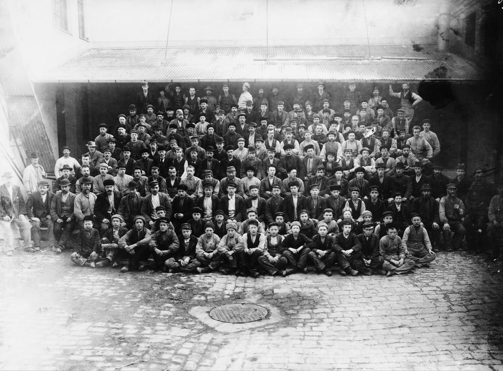 Fabrikkarbeidarar ved Christiania Guldlistefabrikk. Vi ser heile arbeidsstokken. Det er berre menn, og dei som sit fremst, er tenåringar og unge gutar. Svart-kvitt-foto.