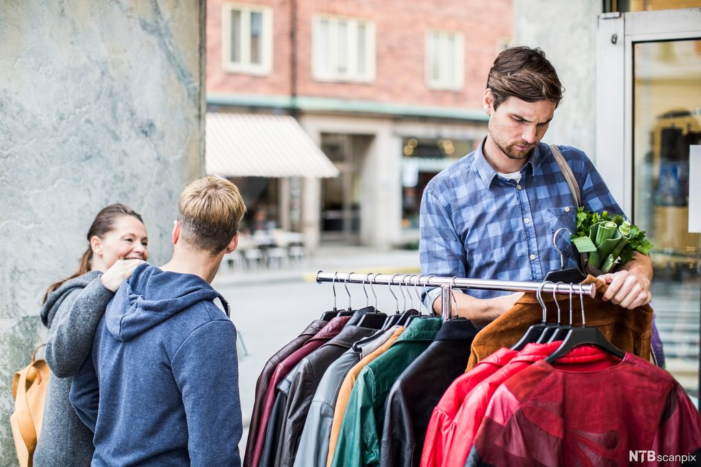 En mann vurderer jakker som henger på et klesstativ utenfor en butikk. Foto.