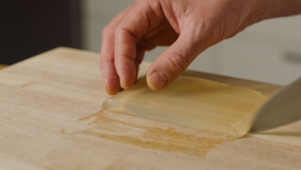 Et stykke nesten gjennomsiktig gelé skjæres i mindre biter på ei trefjøl. Foto.
