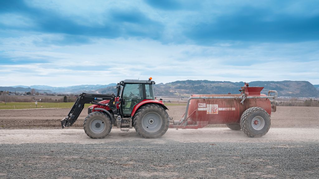 Traktor med gjødselvogn på eit jorde. Foto.