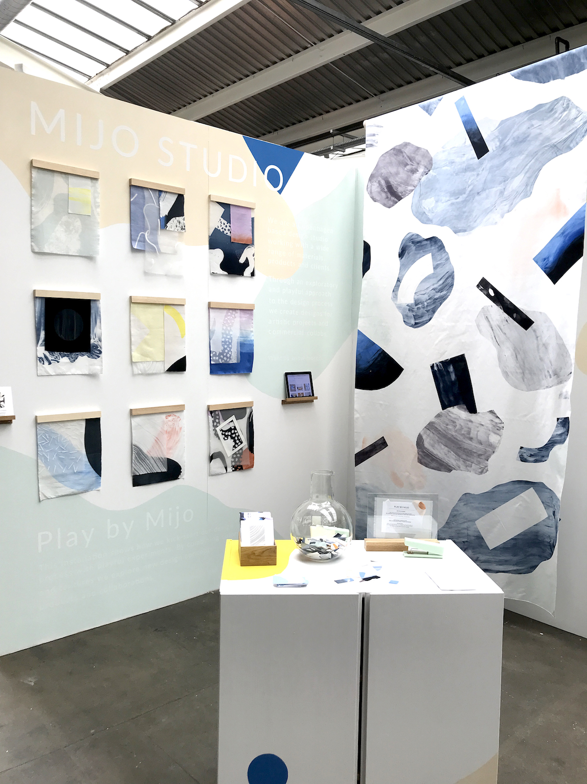 Fotografi av messestand med ulike tekstiltrykk og en benk med fargeprøver. 