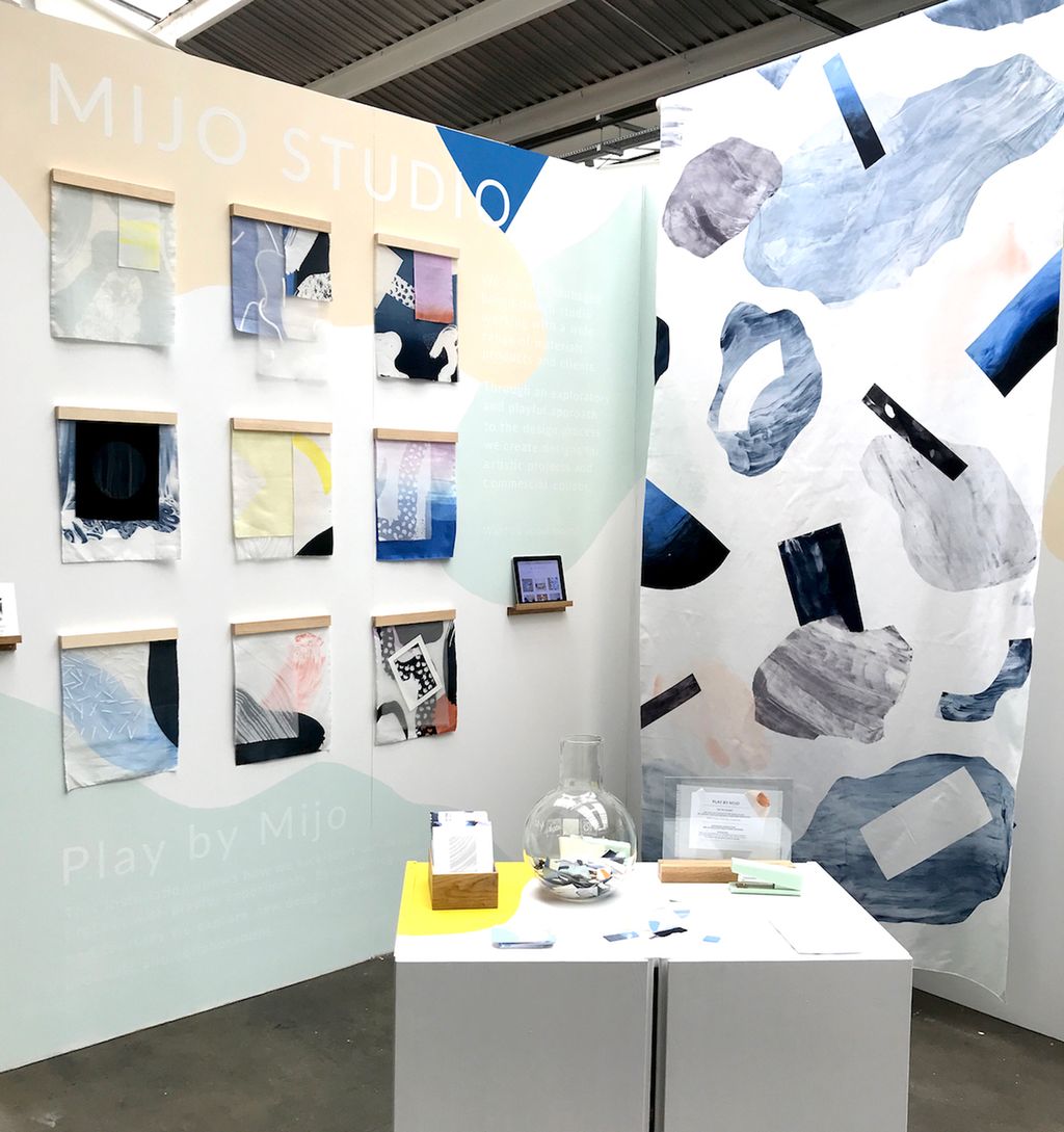 Fotografi av messestand med ulike tekstiltrykk og en benk med fargeprøver.