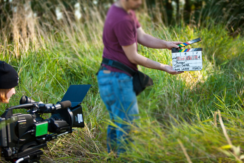 To unge filmfolk skyt ei filmscene ute i naturen. Dei er på ei slette med høgt gras. Foto.