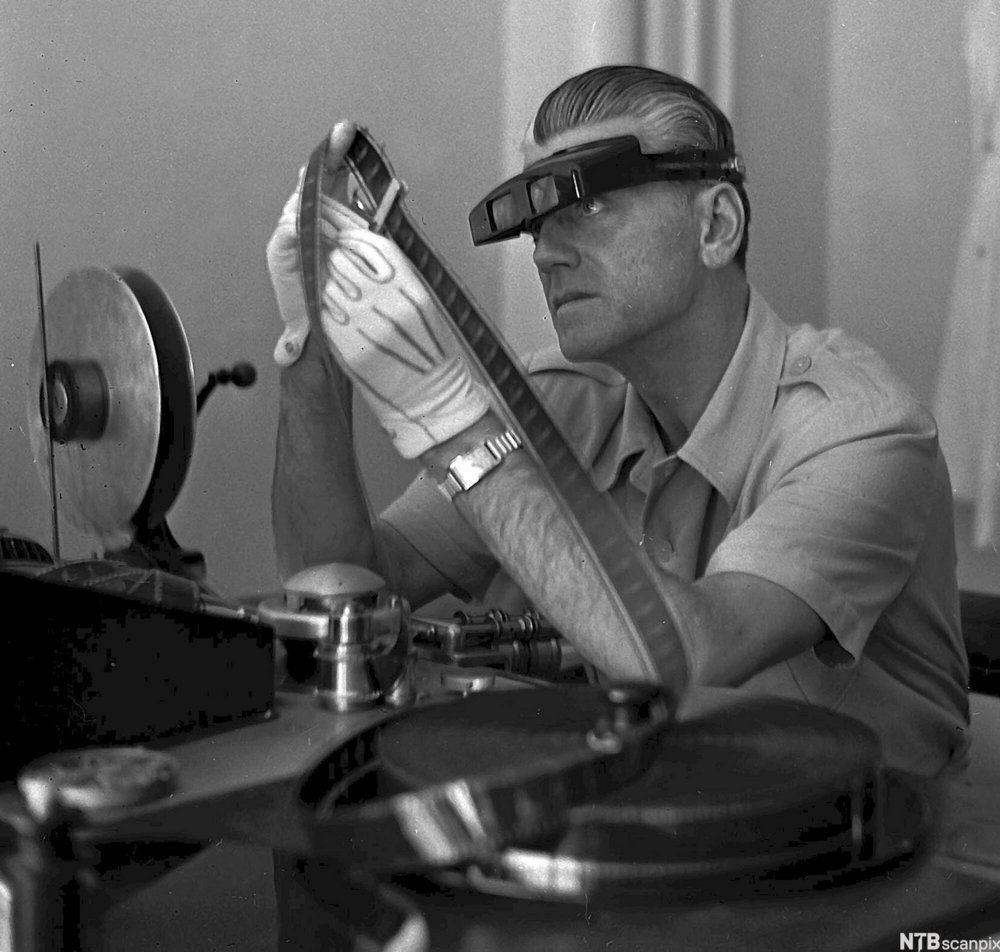 Filmregissør Tancred Ibsen sitter ved klippebordet og studerer en film fra rull. Foto.