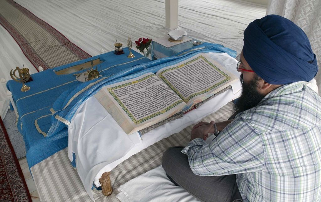 En mann med turban foran en oppslått bok som ligger på et hvitt klede. Foto