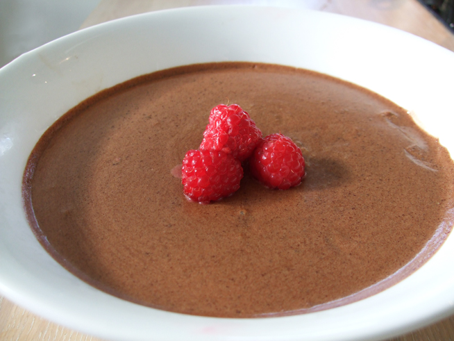 Sjokolademousse i en hvit skål, pyntet med friske bringebær. Foto.
