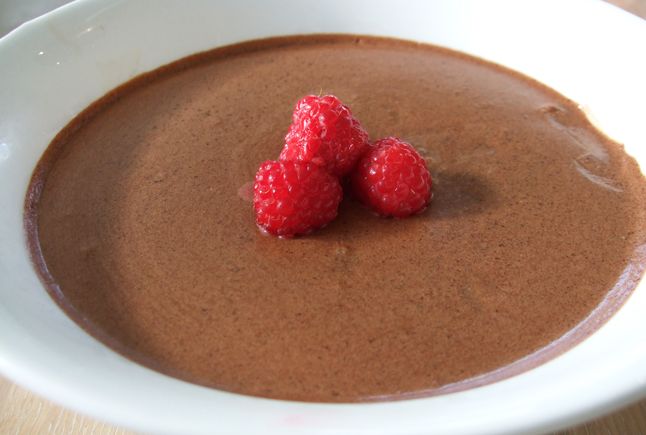 Sjokolademousse i en hvit skål, pyntet med friske bringebær. Foto.