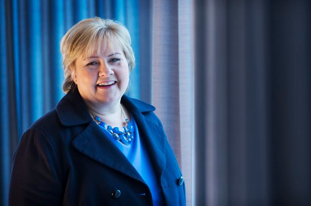 Smilende kvinne i blå genser og jakke. Portrett av Erna Solberg. Foto. 
