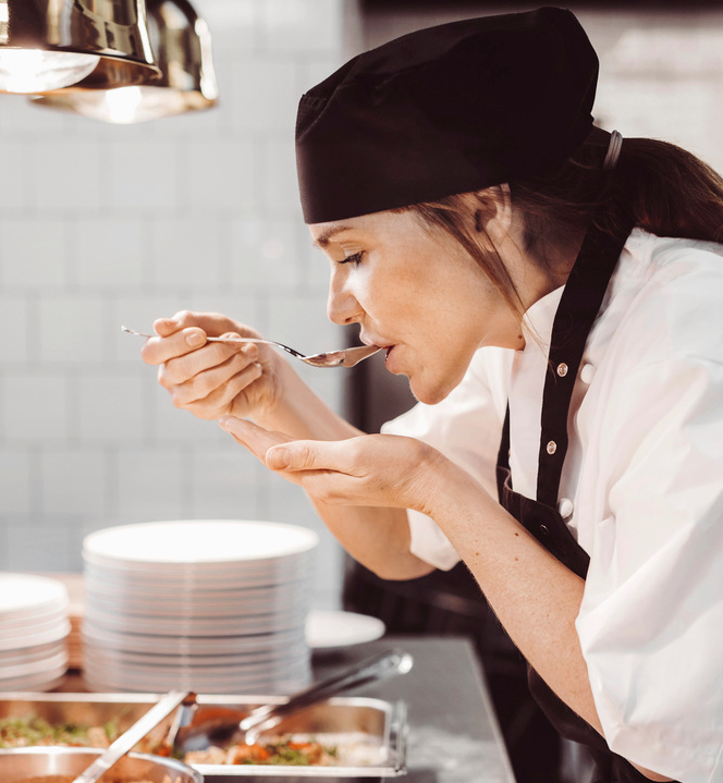 Ein kokk smakar på maten med ei skei. Foto.