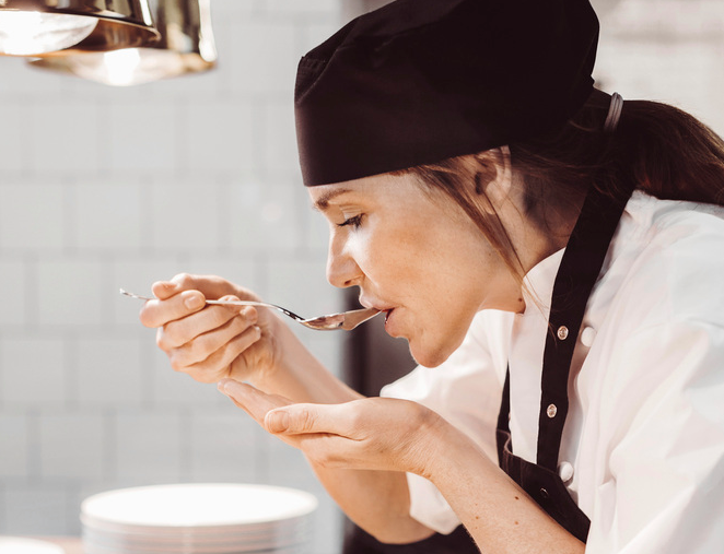 Ein kokk smakar på maten med ei skei. Foto.
