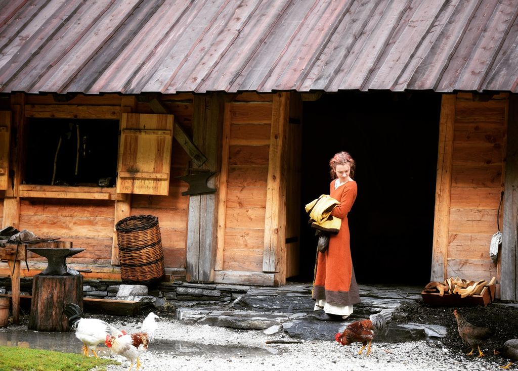En ung vikingkvinne utenfor hjemmet sitt, en trebygning. Foto.