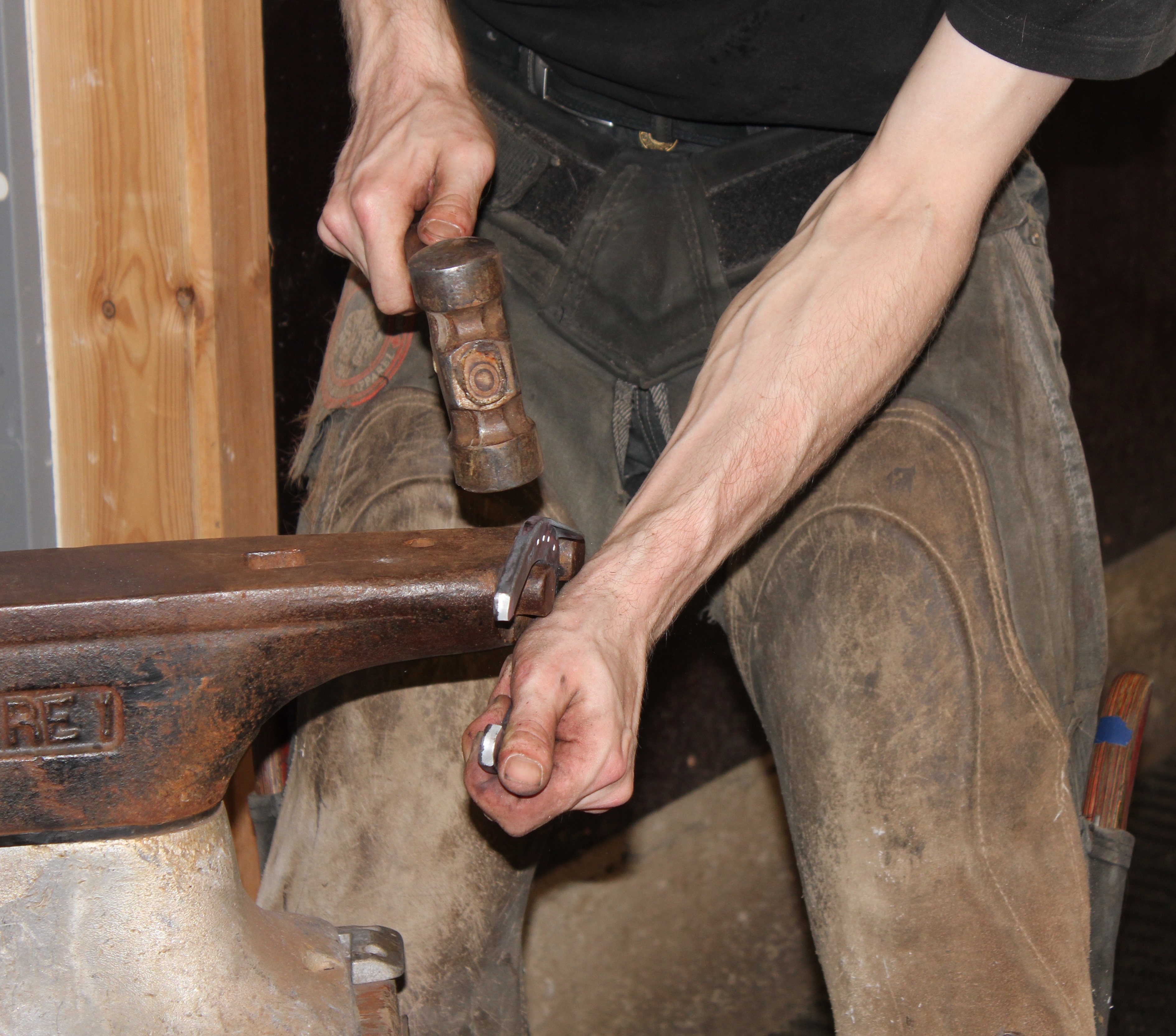 En smed bruker smihammer til å forme metall på en ambolt. Foto.