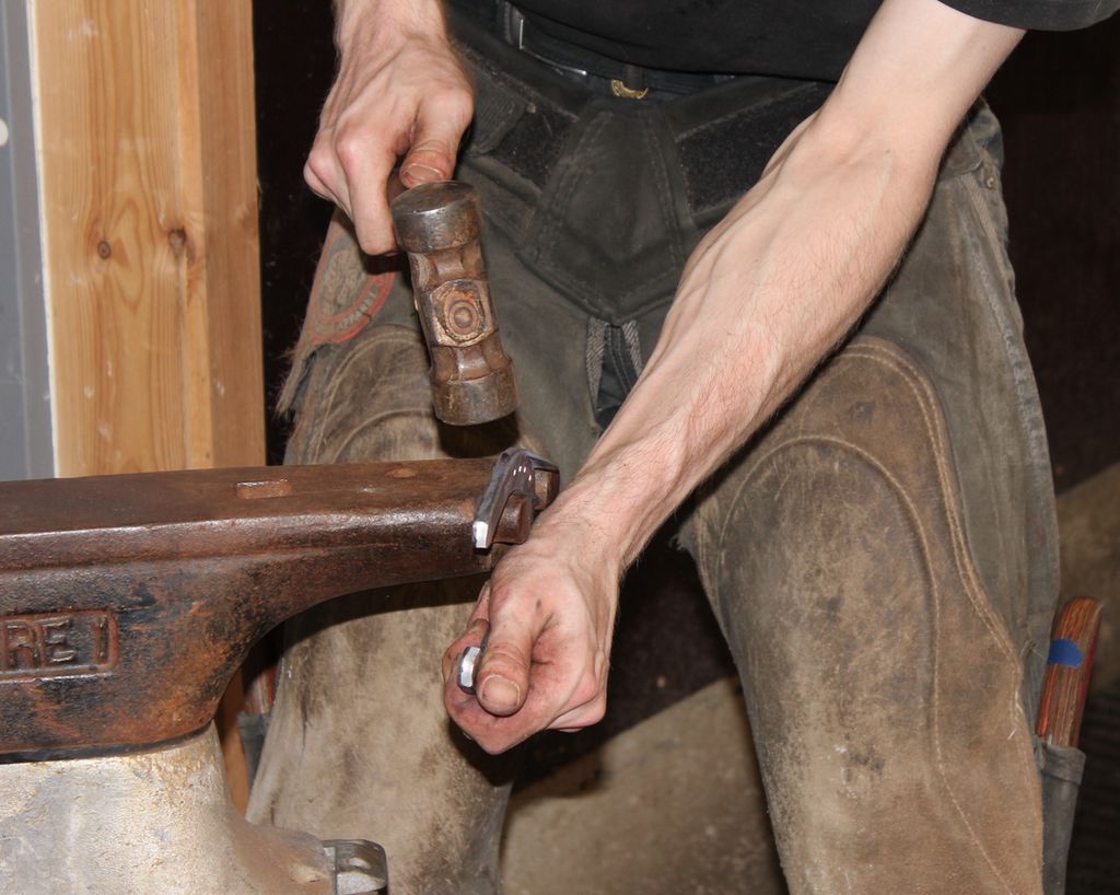 En smed bruker smihammer til å forme metall på en ambolt. Foto.