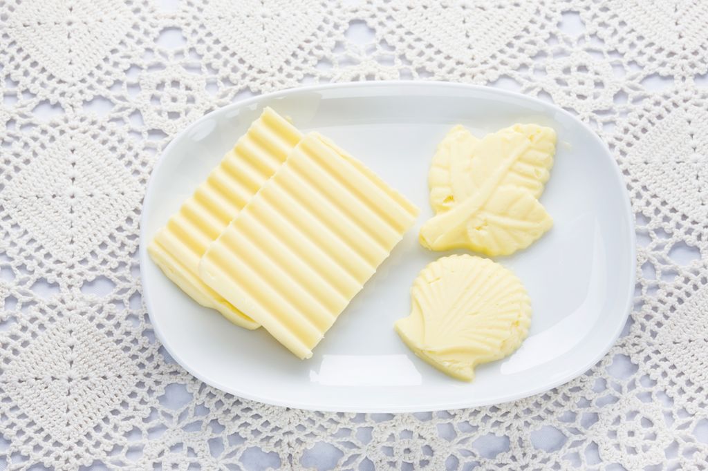 Smør i ulike former på en hvit asjett. Foto.