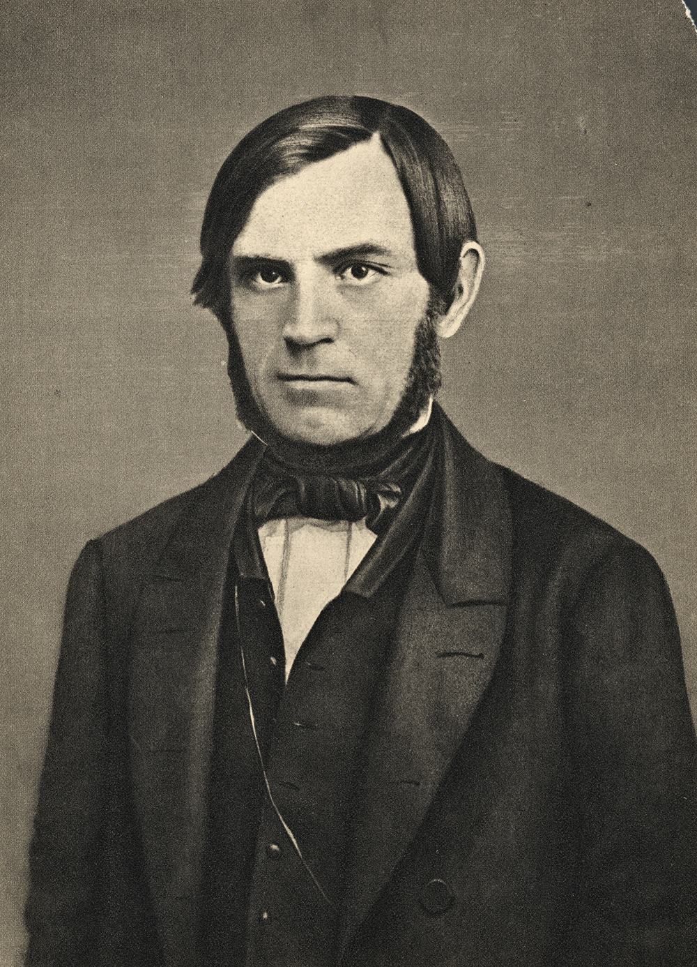Portrett av Søren Jaabæk. Han har mørkt hår og er glattbarbert i ansiktet, men har skjegg i en krans fra foran ørene og  inn under haka. Han er kledd i dress med vest og har tørkle i halsen. Foto.