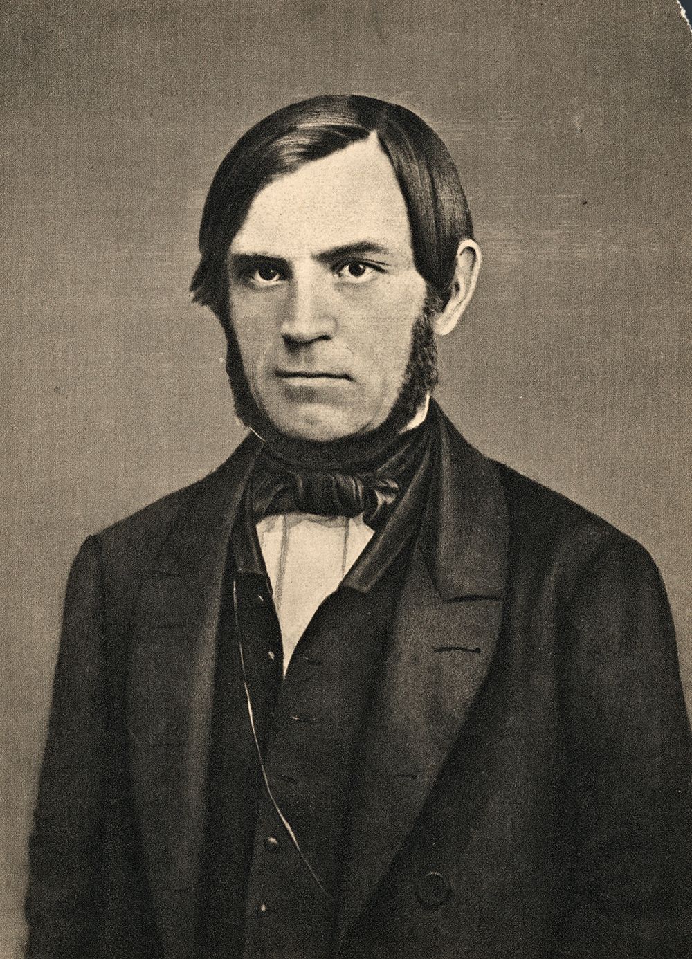 Portrett av Søren Jaabæk. Han har mørkt hår og er glattbarbert i ansiktet, men har skjegg i ein krans frå framfor øyra og inn under haka. Han er kledd i dress med vest og har tørkle i halsen. Foto.