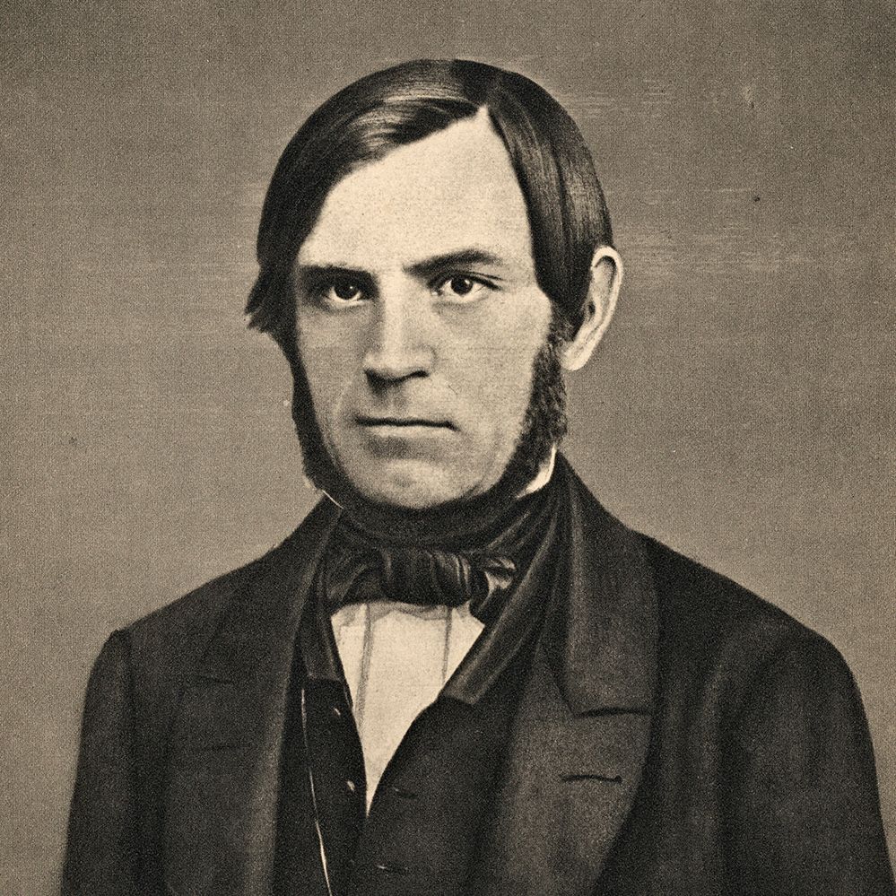 Portrett av Søren Jaabæk. Han har mørkt hår og er glattbarbert i ansiktet, men har skjegg i en krans fra foran ørene og inn under haka. Han er kledd i dress med vest og har tørkle i halsen. Foto.