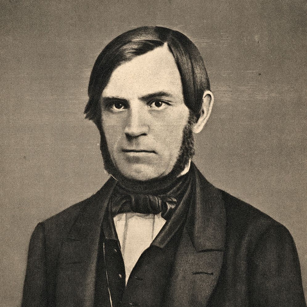 Portrett av Søren Jaabæk. Han har mørkt hår og er glattbarbert i ansiktet, men har skjegg i ein krans frå framfor øyra og inn under haka. Han er kledd i dress med vest og har tørkle i halsen. Foto.