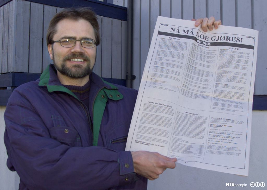 Mann som viser fram ei avisside med tittelen: Nå må noe gjøres! Tittelen er satt med veldig store bokstaver. Foto.