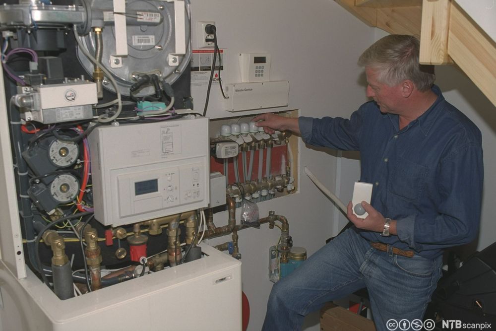 Mann inspiserer sentral for varmeanlegg. Foto.