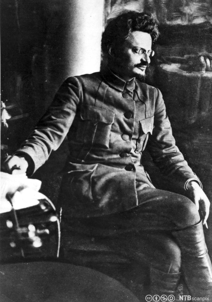 Lev Trotskij iført uniformsjakke med brystlommer. Han har kort, mørkt hår og briller. Foto.