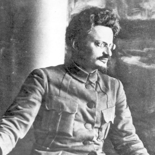 Lev Trotskij iført uniformsjakke med brystlommer. Han har kort, mørkt hår og briller. Foto.