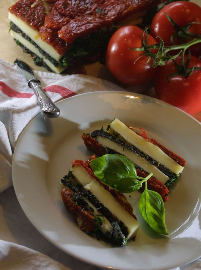 Lag av tomatar og mozzarella pressa saman i avlange serveringsstykke. Lagt til på ein kvit tallerken. Foto.