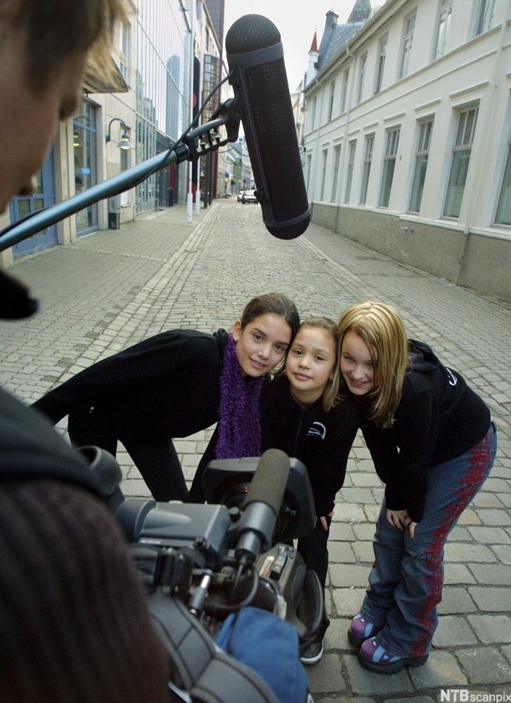 Tre jenter står på ei gate og blir filma. Nokon held ein lydbom over dei. Foto.