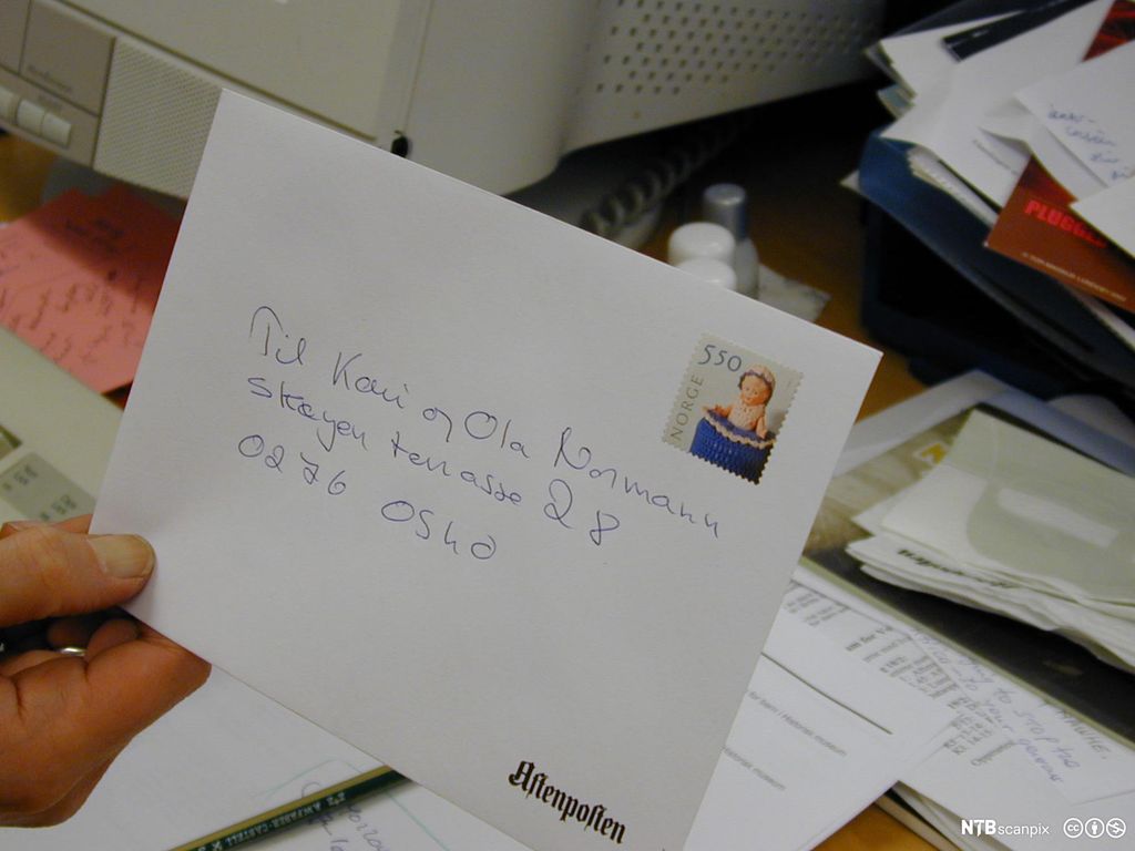Nærbilde av hvit A5-konvolutt med handskrevet adresse og frimerke på.